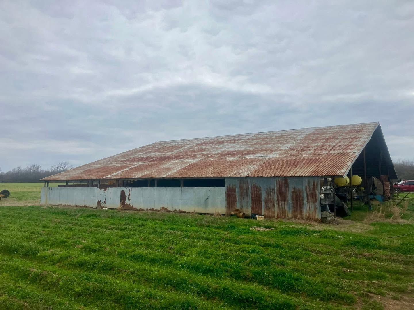 Long open-sided barn with a rusted metal roof before coating