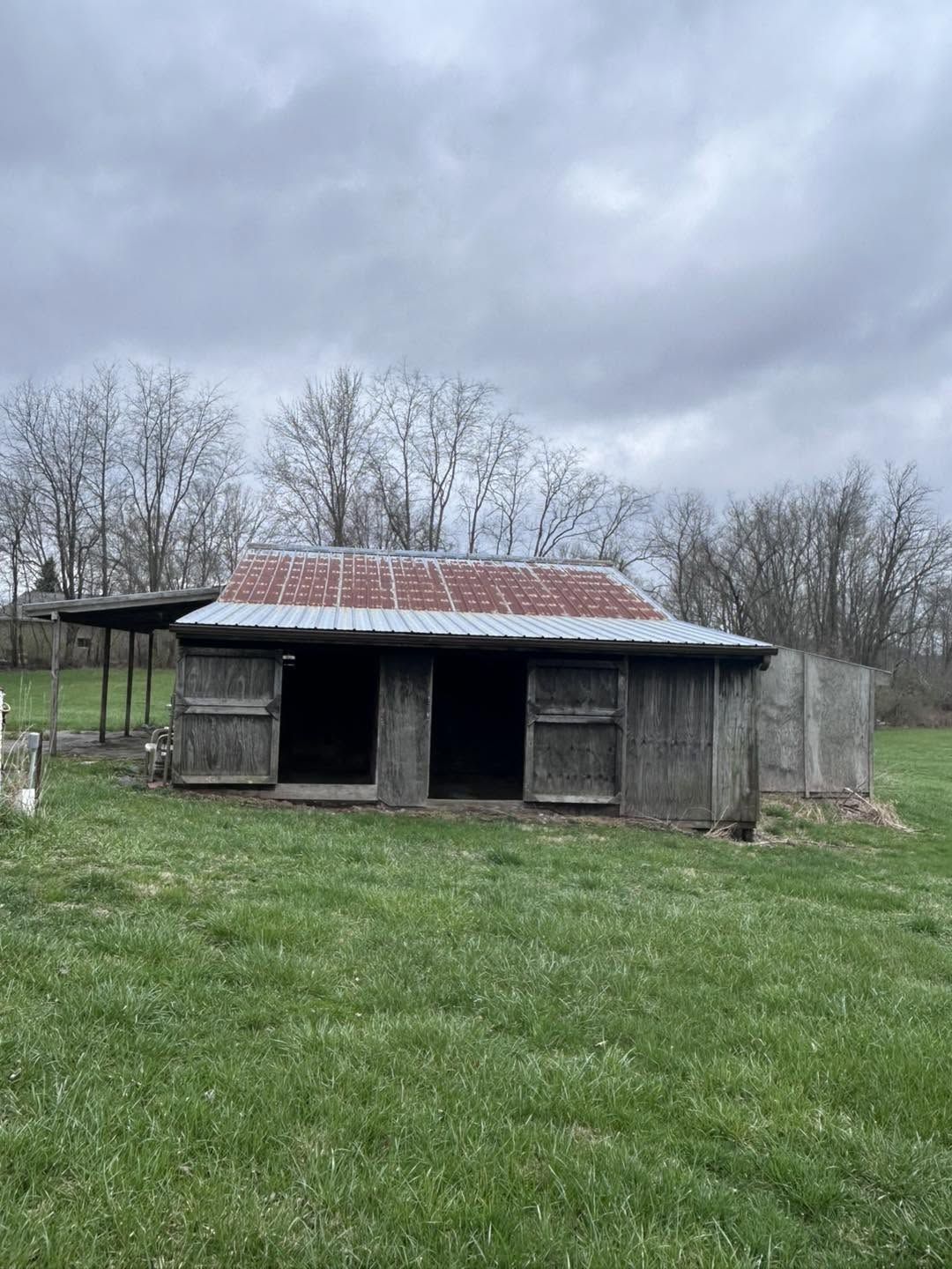 Small wooden barn with a rusted metal roof before coating